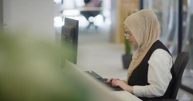 In a modern office, a Muslim entrepreneur wearing a hijab sits confidently and diligently works on her computer, embodying determination, creativity, and empowerment in the business world video