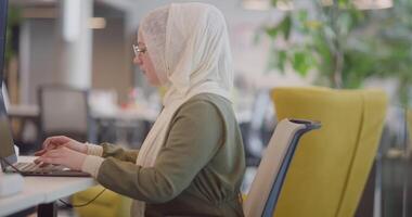 A businesswoman in a hijab is seen working on a computer in a modern office, highlighting inclusivity and professionalism in a diverse workplace video
