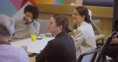 A diverse team of business experts in a modern glass office, attentively listening to a colleague's presentation, fostering collaboration and innovation video