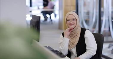 In a modern office, a Muslim entrepreneur wearing a hijab sits confidently and diligently works on her computer, embodying determination, creativity, and empowerment in the business world video