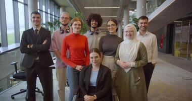 A diverse group of young business professionals stands confidently and looks into the camera in a modern business center, symbolizing ambition, diversity, and a forward-thinking corporate culture video