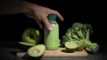 Fresh green smoothie in bottles, hand picking up smoothie from wooden board. Ingredients include avocado, lime, broccoli apple cucumber Great for detox and health-focused content. Enjoy this smoothie video