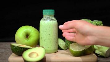 sano verde zalamero en botellas, mano cosecha arriba zalamero desde de madera tablero en mesa. caracteristicas palta, Lima brócoli manzana Pepino ideal para bienestar y relacionado con la nutrición Perfecto zalamero elección video