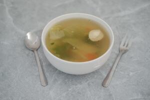 A bowl of soup with a spoon and fork on a wooden table photo