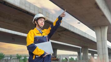 Asian female civil engineer using laptop computer standing on road construction site to supervise the construction of a new road. photo