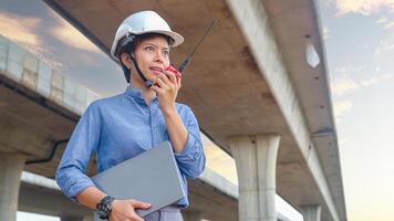 Asian female engineer using walkie talkie at construction site Standing near the concrete road, highway bridge. photo