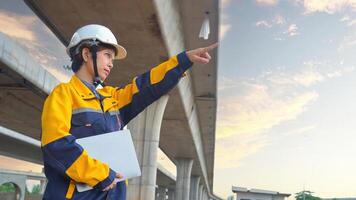 Asian female civil engineer using laptop computer standing on road construction site to supervise the construction of a new road. photo