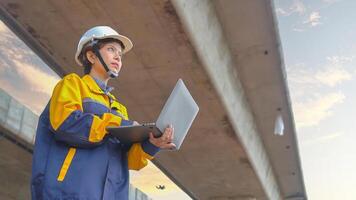 Asian female engineer Wear a yellow safety suit. Use a laptop to inspect highway construction work. photo