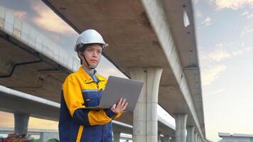 Asian female engineer Wear a yellow safety suit. Use a laptop to inspect highway construction work. photo