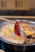 A pair of hands use wood chopsticks put thinly sliced meat in hot boiled photo