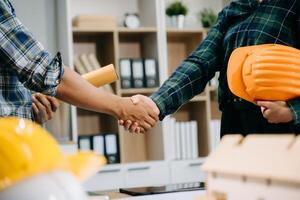 Construction team shake hands greeting start new project plan behind yellow helmet on desk in office center to consults about their building project. photo