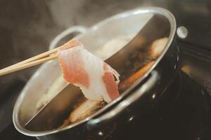 Man hand takes raw delicious pork slices of high quality with put cooking in hot boiled soup photo