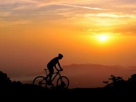 Silhouette of a Cyclist Riding a Mountain Bike at Sunset with Scenic Landscape in the Background photo