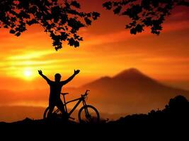 Silhouette of Cyclist with Bicycle Celebrating at Sunset with Mountain in Background photo