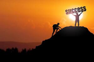 Silhouette of Two Climbers Reaching the Peak with Success Banner at Sunset photo