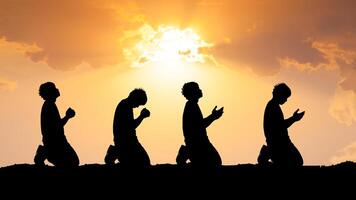 Silhouetted Figures Praying at Sunset with Dramatic Sky and Sunlight in the Background, Capturing Spirituality, Devotion, and Peaceful Reflection in a Serene Outdoor Setting photo
