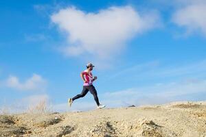 Man Running on a Rocky Trail Under a Clear Blue Sky with White Clouds in the Background photo