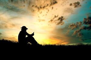 Silhouette of a Person Sitting on Grass at Sunset with Dramatic Sky and Clouds in the Background photo