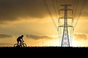 Silhouette of Cyclist Riding Bike at Sunset with Power Lines in Background, Scenic Evening Sky, Outdoor Adventure, Energy Infrastructure, Tranquil Landscape, Golden Hour Photography photo