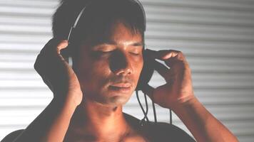 Young Man Enjoying Music with Headphones in a Relaxed Setting, Eyes Closed, and Peaceful Expression, Against a Striped Background, Highlighting the Joy and Tranquility of Listening to Music photo