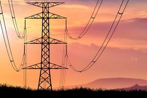 Silhouette of High Voltage Power Lines and Transmission Tower at Sunset with Vibrant Sky and Mountains in the Background photo