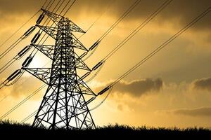 Silhouette of High Voltage Power Lines and Transmission Tower at Sunset with Dramatic Sky and Clouds in the Background, Symbolizing Energy, Electricity, and Infrastructure photo