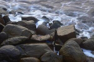 Large boulders hit by the waves around the beach photo