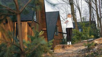 A woman doing morning exercises near a wooden hut surrounded by trees, enjoying the fresh air and morning light, symbolizing a healthy and active lifestyle in a natural environment video