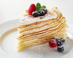 a piece of crepe cake with berries and powdered sugar photo