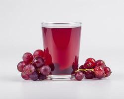a glass of red grape juice with some grapes photo