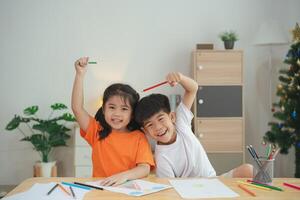 Two children are sitting at a table with crayons and drawing paper. One of the children is holding a pencil and the other is holding a crayon. They are both smiling and seem to be enjoying themselves photo