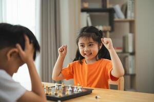 A girl in an orange shirt is playing a game of chess with a boy. The girl is smiling and he is enjoying the game photo