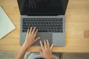A child is typing on a laptop with a keyboard and a mouse. The child is sitting on a chair and is focused on the laptop photo