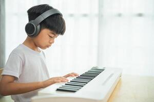 A young boy is playing the keyboard with headphones on. He is focused on the music and he is enjoying himself photo