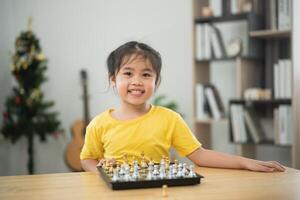 Asian young girl is sitting at a table with a chess board in front of her. She is smiling and she is enjoying herself photo