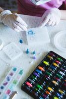 Children's hands in gloves fill an epoxy resin ring mold with decorative sparkles vertical view photo