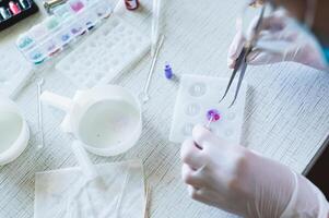 Female hands in gloves fill an epoxy resin button mold with decorative elements photo