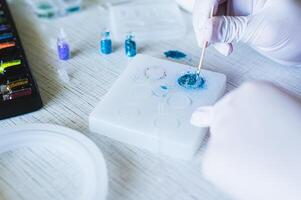 Children's hands in gloves fill an epoxy resin ring mold with decorative sparkles photo