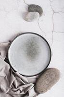 Empty ceramic plate, stones and napkin on gray background top and vertical view photo