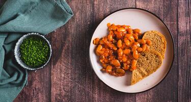 Plate with baked beans in tomato sauce and rye bread on the table top view web banner photo