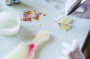 A girl in gloves uses tweezers to place elements into a mold for making earrings from epoxy resin photo