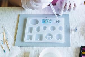 Children's hands in gloves fill a mold for making a puzzle piece with epoxy resin photo