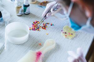 A girl in gloves uses tweezers to select decorative elements for making earrings from epoxy resin photo