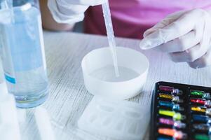Female hands in gloves squeeze epoxy resin from a pipette into a bowl for making jewelry photo