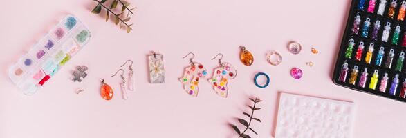 Earrings, pendants and rings made of epoxy resin, mold and sparkles on a pink top view web banner photo