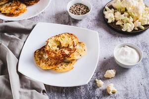 Homemade cauliflower fritters on a plate and sour cream in a bowl on the table photo