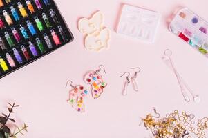 Earrings made of epoxy resin, molds and sparkles for making on a pink background top view photo
