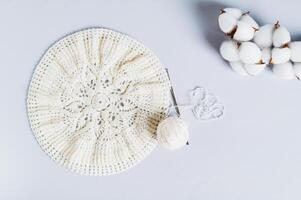 An uncrocheted beret, a ball and a cotton branch on a blue background top view photo