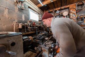 A senior man procesing wood on a lathe and making wooden dishes in the workshop photo