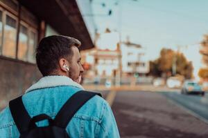 Back view of a man listening to music and talking on wireless headphones in the city center photo